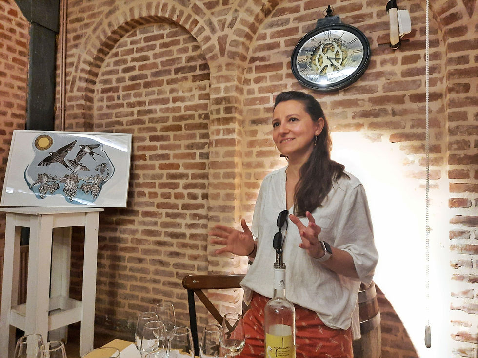 Turkish woman winemaker standing with open hands in front of a brick wall with wine in front of her