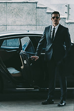 man in suit is holding a door open to a black car