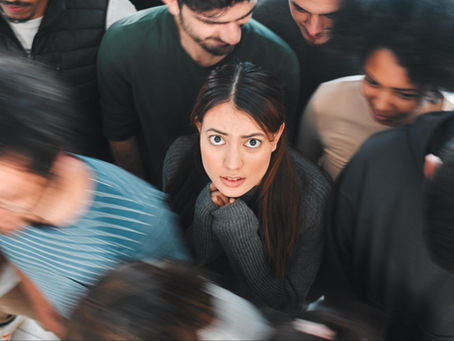 A young woman surrounded by people looks anxious, showing visible signs of psychological distress.