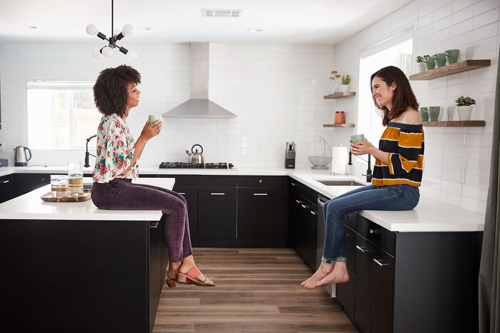 Two women sitting on countertops and holding mugs. 