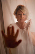 Portrait von Lara, sie hält die Hand zum Distanz wahren, verdeckt hinter einem Mückennetz.