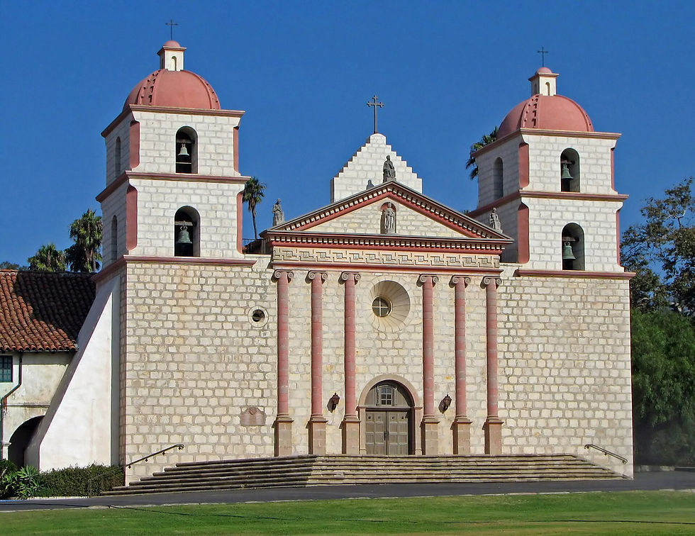 The pink and cream facade and twin bell towers of Old Mission Santa Barbara under a blue sky