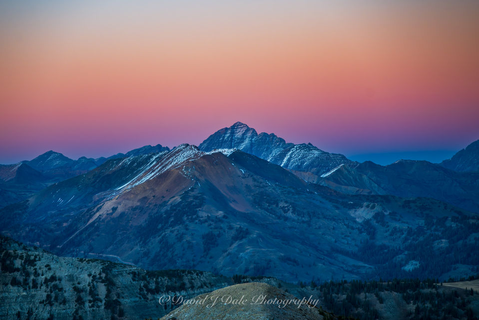 Twilight in the mountains brings out deep orange and purple color in the sky while a fresh dusting of snow on the distant peaks creates a beautiful post sunset scene.