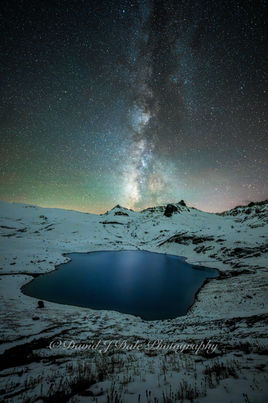 Milky Way rising above high alpine lake with snow covered mountain landscape and turquoise blue water