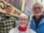Three people smiling in front of Wilkes County Mural highlighting MerleFest and music
