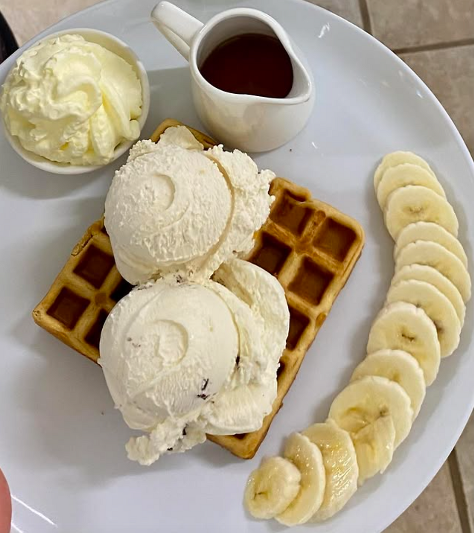 Waffle topped with vanilla ice cream on a plate with sliced bananas, whipped cream, and syrup in a jug. Light, creamy, and inviting.