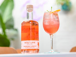 Wolf Lane Grapefruit Aperitif bottle and spritz cocktail garnished with fresh grapefruit, perfect for summer sipping in the tropics.