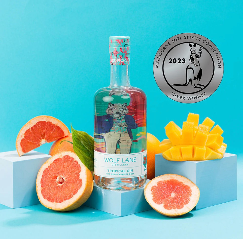 Bottle of Wolf Lane Tropical Gin surrounded by sliced grapefruit and mango against a blue background. Silver award badge visible.