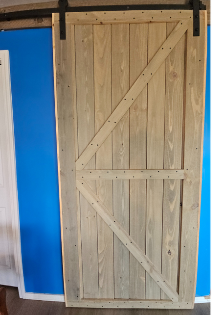 Handcrafted wooden barn door with Z-brace design and black sliding hardware, installed against a bright blue wall.