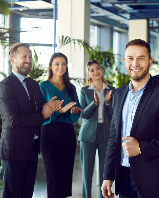 Smiling young attractive boss and business leader man proudly looking at camera with team