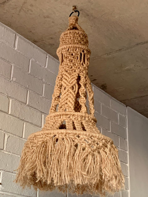 a macrame lamp hanging from the ceiling in front of a white brick wall