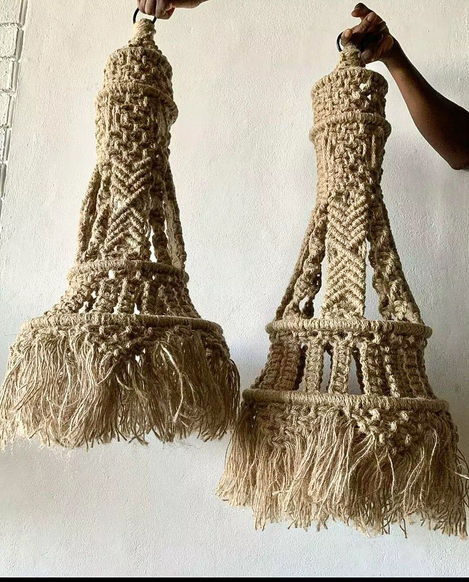 a person is holding a pair of macrame lamps against a white wall .
