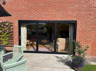 Black bifold doors leading to a rear garden with chairs