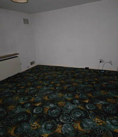 Unfurnished room with dark green patterned carpet requiring property clearance services.