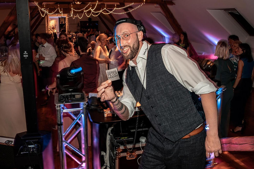 DJ Jan Mitchell lächelt hinter dem DJ-Pult auf einer Hochzeitsfeier in die Kamera.