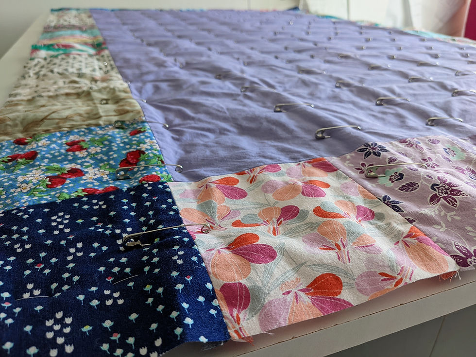 Close up shot from the corner of an ironing mat prepped for machine quilting. The border is made of squares of fabrics in different patterns around a lavender center rectangle.