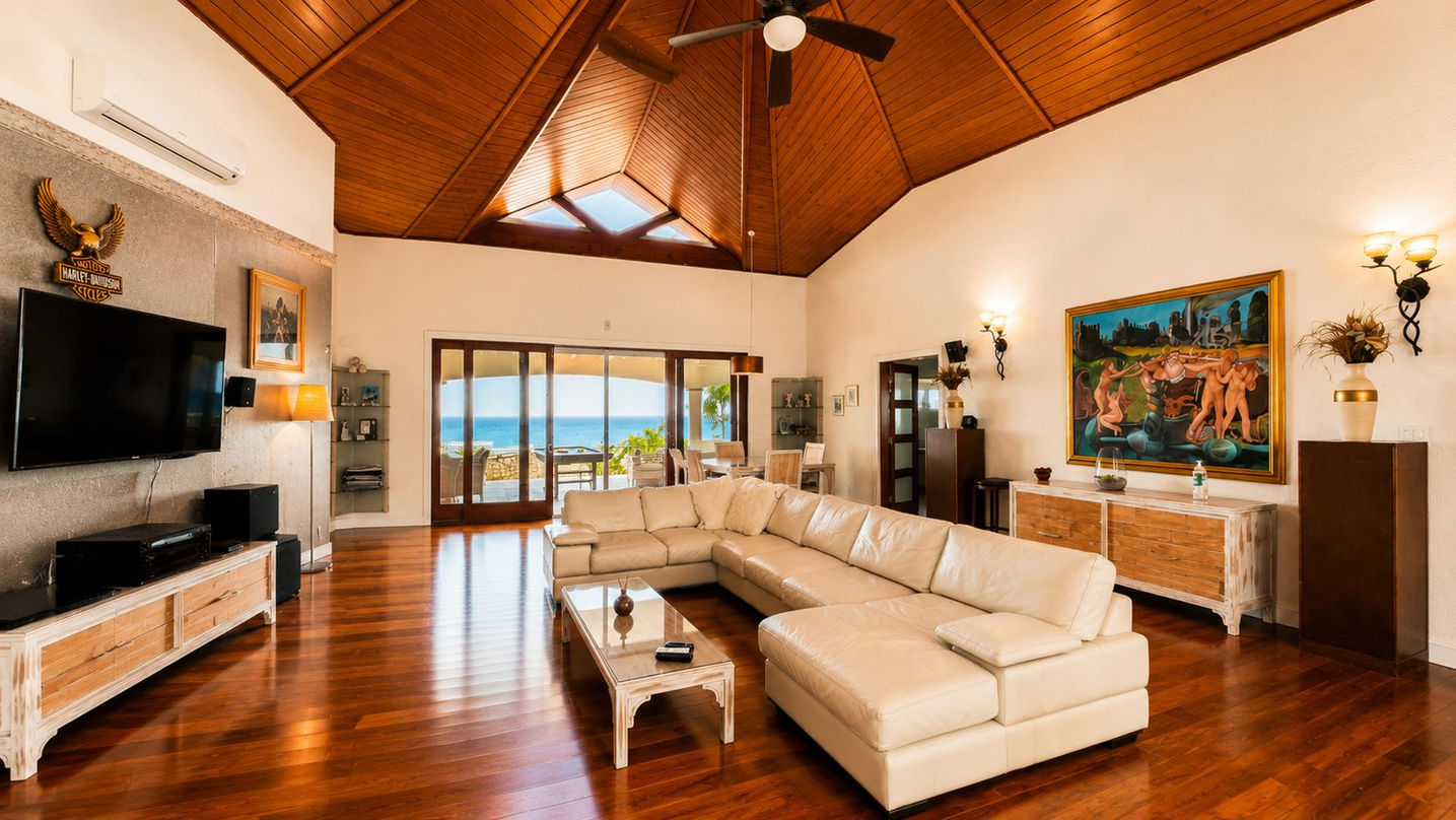 Spacious open-concept living room with vaulted wood ceilings, premium furnishings, hardwood floors, and panoramic Caribbean Sea views in St. Maarten.