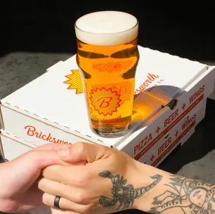 A beer sitting on top of pizza boxes while two people thumb wrestle in the foreground