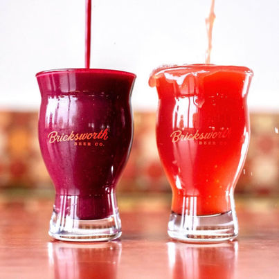 two fruited beers, one purple, and one red, being poured into a glass