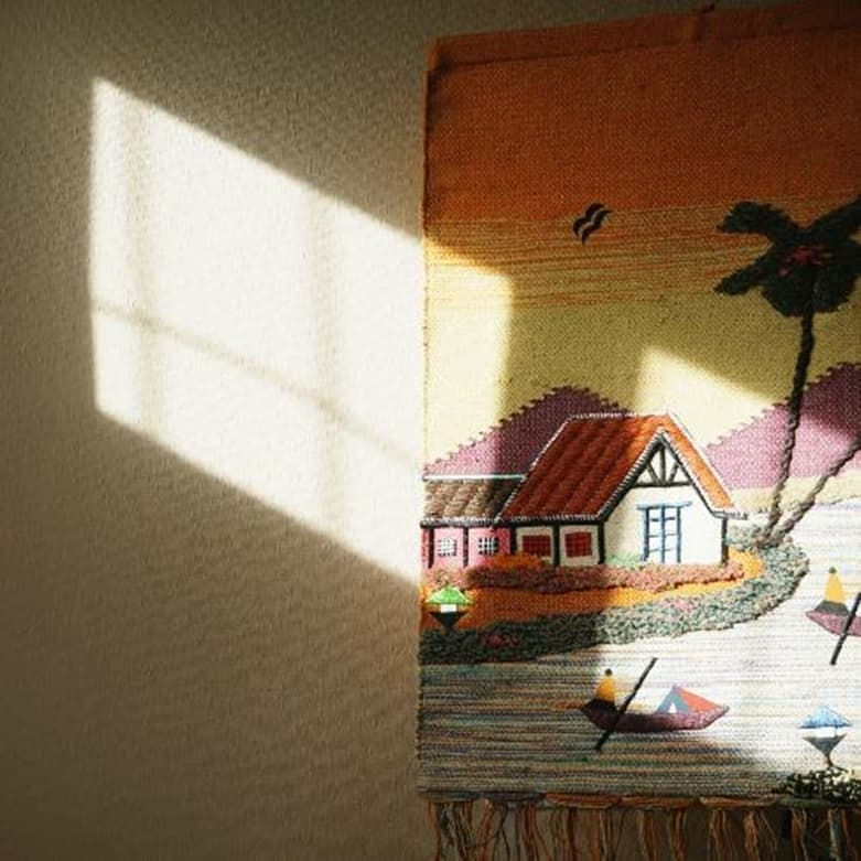 Een muur met daarop behang/kunstwerk, met een huis en een palmboom