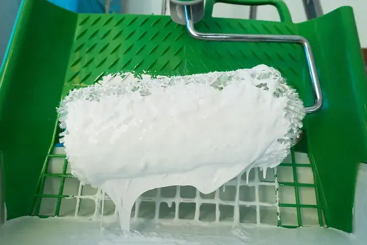 Witte verf op een roller in een groene bak
