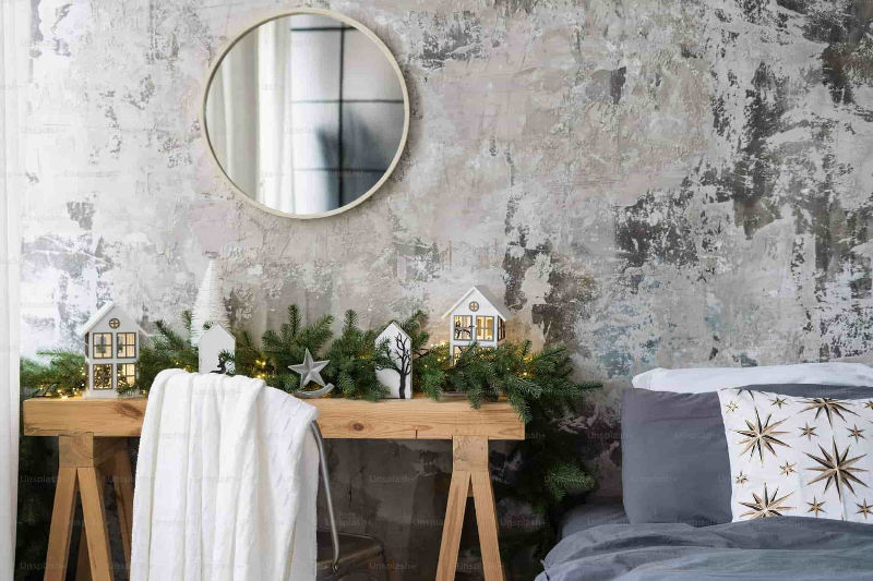 Muur met spiegel, voor de muur staan een bed en tafeltjes met kerstdecoraties er op.