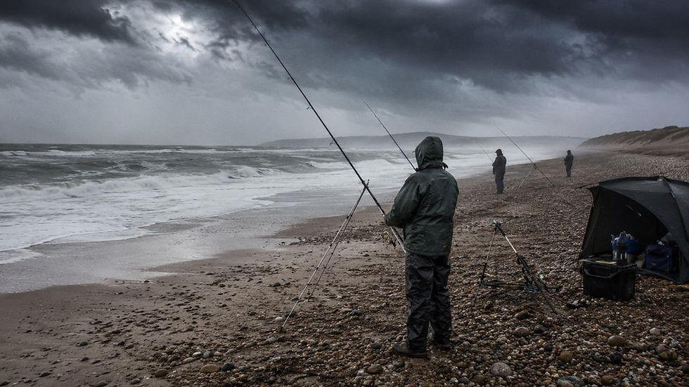 Anglers on a stormy pebble beach hold fishing rods beside a shelter, with rough waves and dark clouds rolling in.