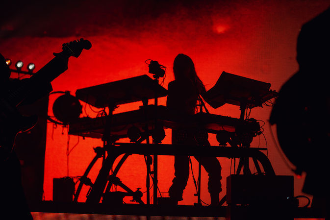 Silhouette of musician with keyboards against red background.