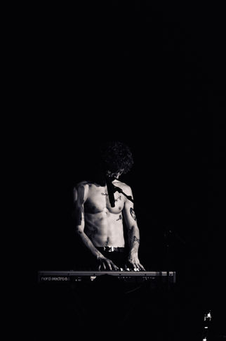 Shirtless person playing keyboard in dark setting.