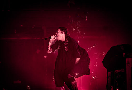 Performer singing passionately on stage with red lighting.