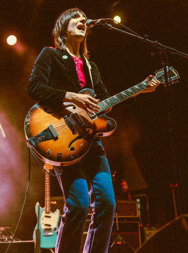 Musician playing guitar on stage with microphone.