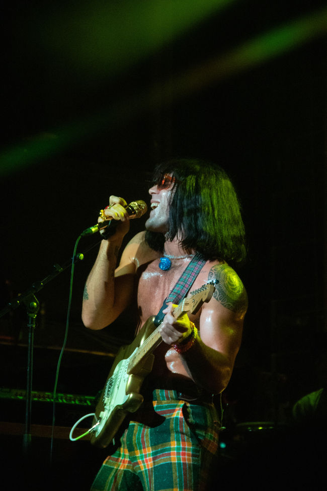 Musician passionately singing and playing guitar on stage.