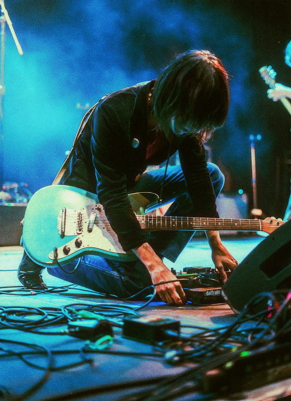 **First Image:** Blue and green abstract geometric shapes.
**Second Image:** Musician adjusting guitar pedals on stage.