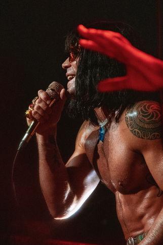 Shirtless man singing passionately on stage.