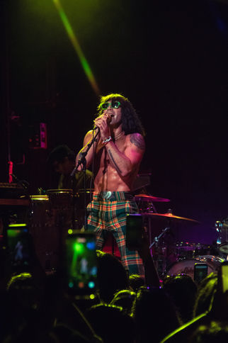Shirtless performer singing on stage with microphone.