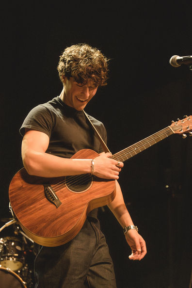 Person playing acoustic guitar on stage, smiling.