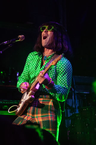 Musician in green shirt and sunglasses playing guitar.