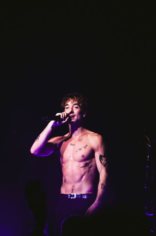Shirtless performer singing on stage with microphone.