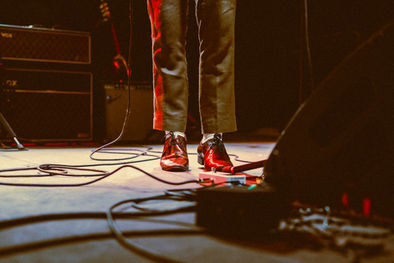 Musician's feet on stage with equipment and cables.
