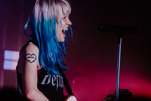 Person with blue hair singing on stage passionately.