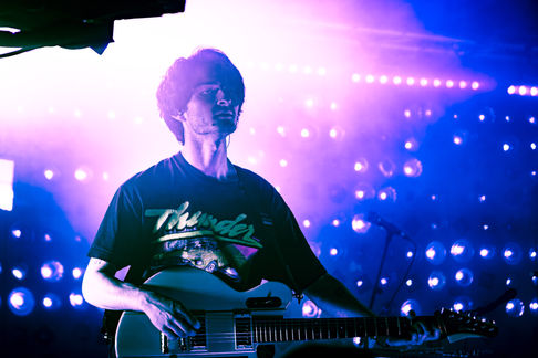 Musician playing guitar under vibrant stage lights.