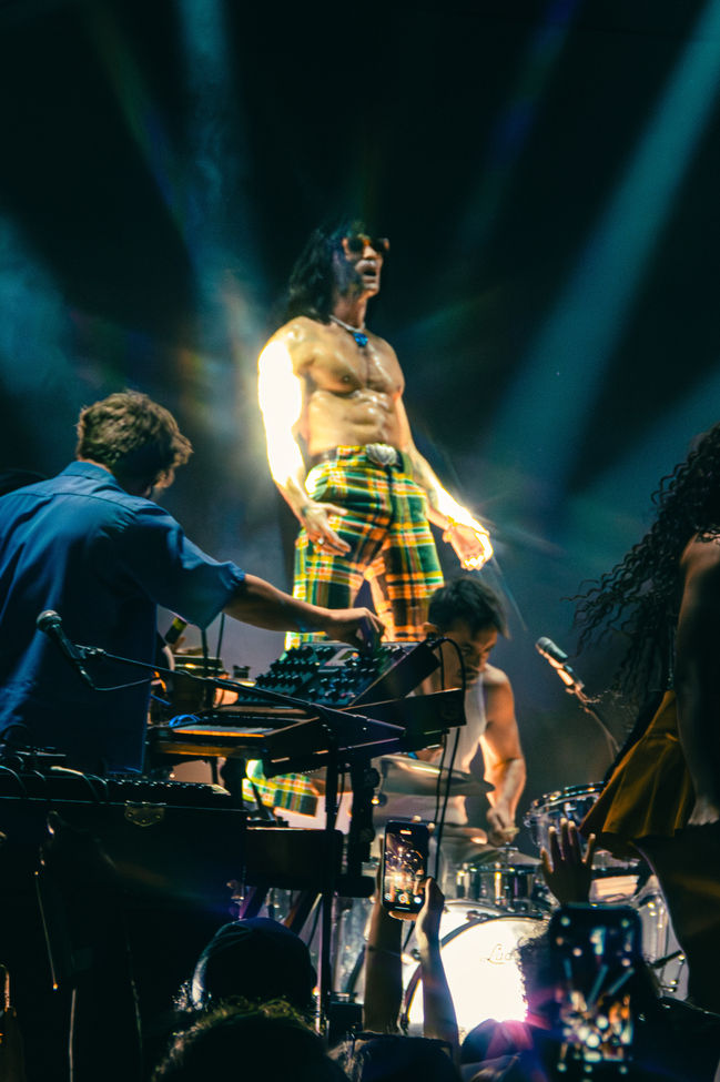 Band performing energetically on stage with colorful lighting.