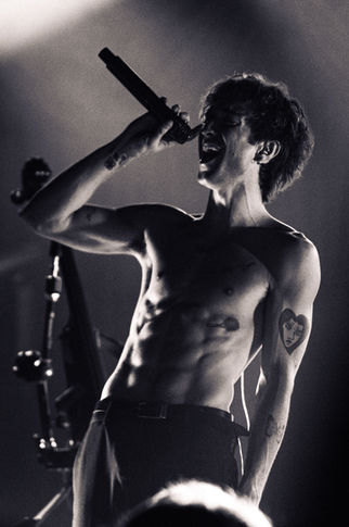Shirtless performer singing passionately on stage.