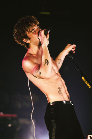 Shirtless singer performing passionately on stage.