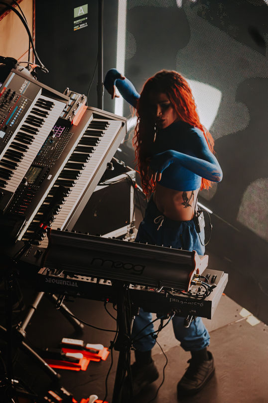 Musician playing keyboards on stage with dramatic lighting.