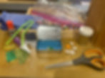Craft supplies on a table: scissors, glue, pipe cleaners, tissue paper, beads, an Altoids tin and a seashell and star accents.