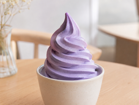 Paarse ube soft serve in een hoorntje met kokos topping op een lichte café achtergrond.