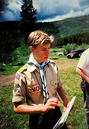 Brandon in Scout uniform looking through papers beside a car after arriving at Camp Tifie.