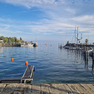 Quiet Meersburg harbor—jetties, buoys and masts reflected in glassy water.