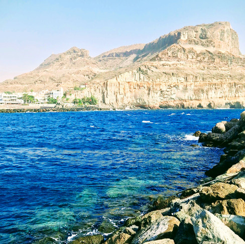 Rocky coastline and clear blue ocean in Puerto Rico, Gran Canaria, with cliffs in the background.